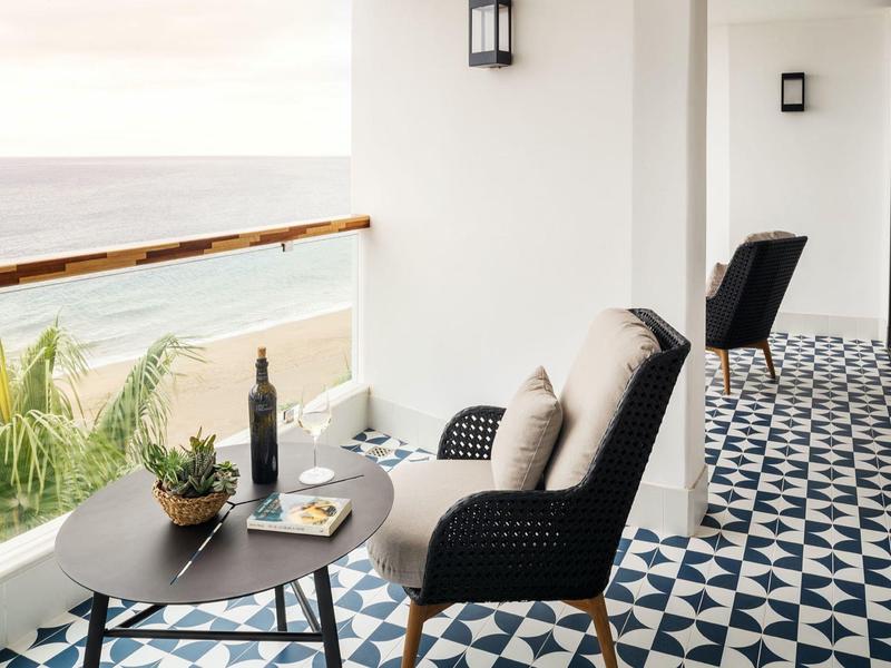 Balcone con sedie, tavolo, bottiglia di vino e vista sul mare con sole.