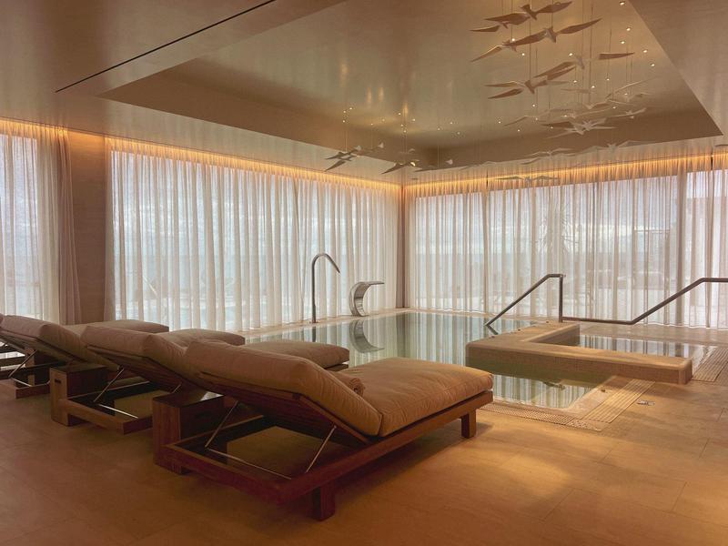 Lounge benessere luminosa con lettini vicino a una piccola piscina interna e grandi finestre.