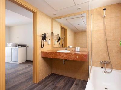 Helles Badezimmer mit braunem Waschtisch, großem Spiegel, Fön und Badewanne mit Duschkopf.