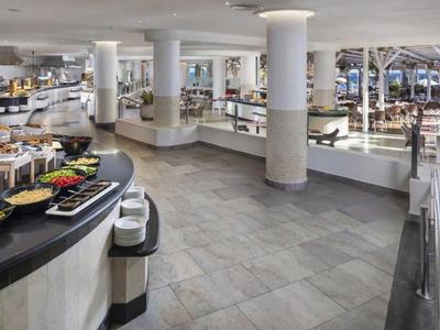 Großer moderner Buffetbereich mit runden weißen Tischen, Säulen und hellem Fliesenboden.