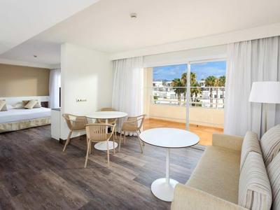 Helles Wohnzimmer mit Holzfußboden, runder Tisch, beige Couch und Zugang zu Terrasse mit Meerblick.
