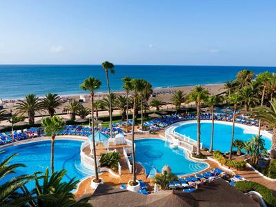 Großer blauer Pool mit Palmen und Liegestühlen am Strand unter klarem Himmel.