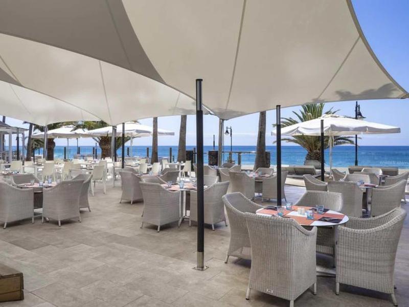Terrazza di ristorante sul mare con ombrelloni bianchi e poltrone in vimini.