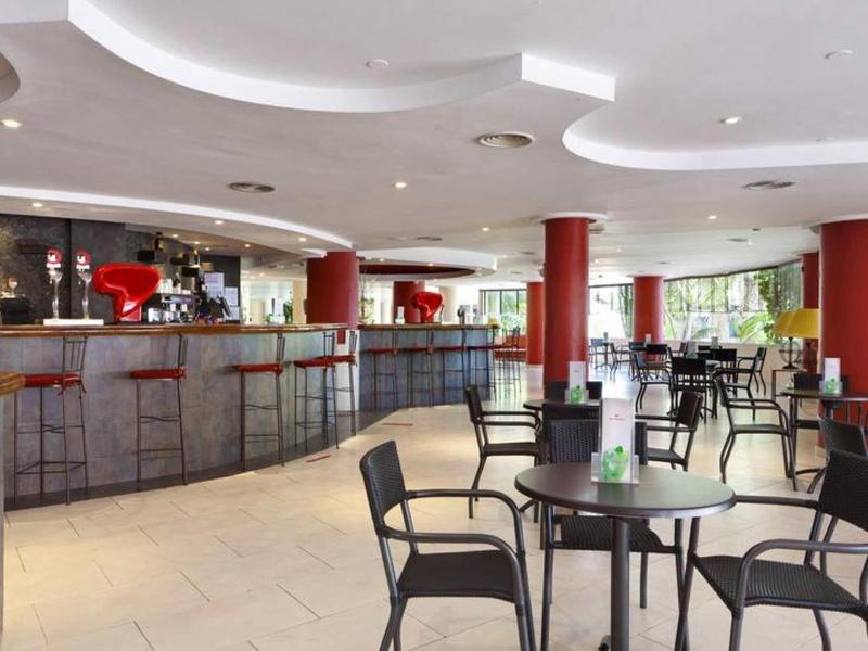 Bar moderno con sedie alte e tavoli rotondi in uno spazio luminoso con pilastri rossi.