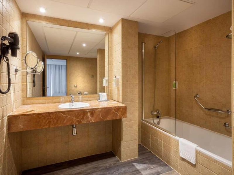 Bagno con lavabo in marmo, grande specchio, vasca beige e pareti piastrellate.