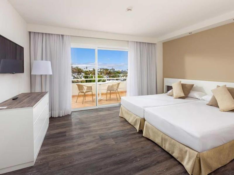 Camera d'hotel luminosa con letto matrimoniale, TV a muro e balcone con vista mare.