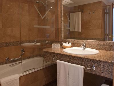 Moderne Badezimmer mit braunen Fliesen, großer Spiegel, Waschbecken und Badewanne mit Glasabtrennung.