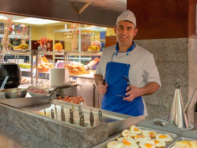 Cuoco con grembiule blu dietro un buffet con vari piatti e uova.