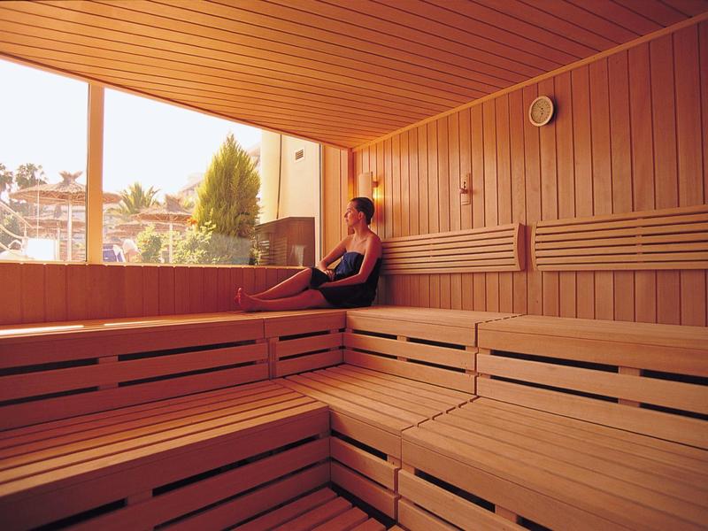 Persona seduta in una sauna di legno con grande finestra e vista esterna.