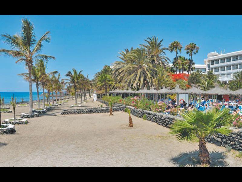 Ampia spiaggia con vista su un grande hotel e palme sotto un cielo azzurro.