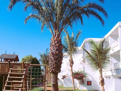 Palme accanto a un parco giochi vicino a un edificio bianco dell'hotel sotto un cielo azzurro limpido.