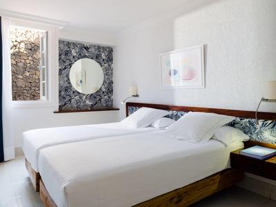 Camera d'albergo luminosa con letti singoli, arredamento moderno e grande specchio su carta da parati floreale.