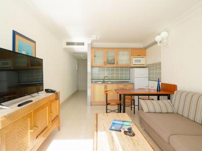 Soggiorno luminoso con divano, TV, tavolo da pranzo e cucina in appartamento vacanze moderno.