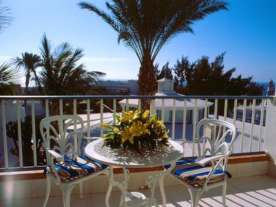 Balcone con tavolo e sedie in metallo bianco con cuscini a righe blu, palme sullo sfondo.