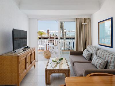 Soggiorno moderno con divano grigio, TV su mobile in legno e balcone con vista mare.