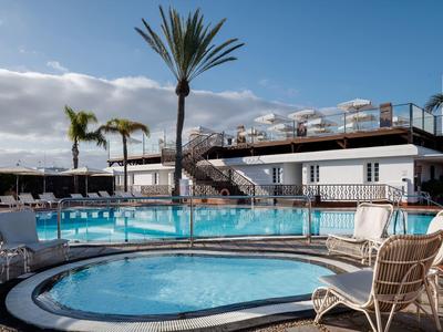 Area piscina esterna con sdraio, ombrelloni e palme in un hotel soleggiato.