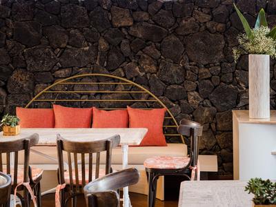 Zona salotto accogliente con sedie di legno, divano con cuscini e piante in vaso davanti a un muro di pietra.