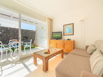 Soggiorno luminoso con divano beige, tavolo in legno e zona pranzo esterna visibile attraverso porte in vetro.