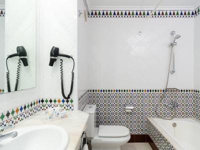 Bagno con decorazioni bianche, piastrelle a motivi, vasca con doccia, lavabo e asciugacapelli a muro.