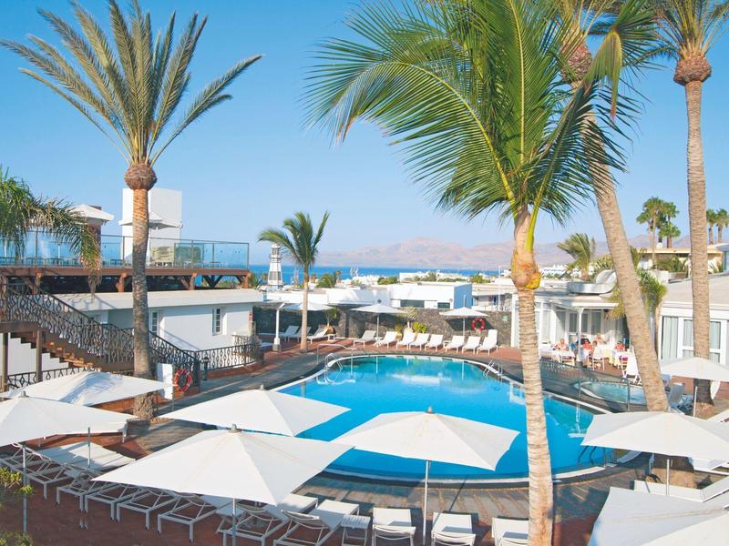 Piscina del resort circondata da ombrelloni, lettini e palme con vista sull'oceano.