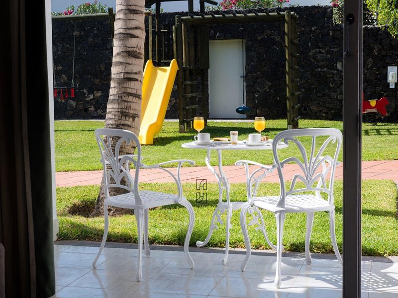 Sedie e tavolo bianchi su un patio con giardino e scivolo giallo sullo sfondo.