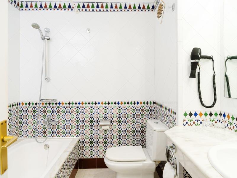 Bagno luminoso con vasca, WC, lavabo e pareti piastrellate decorative.