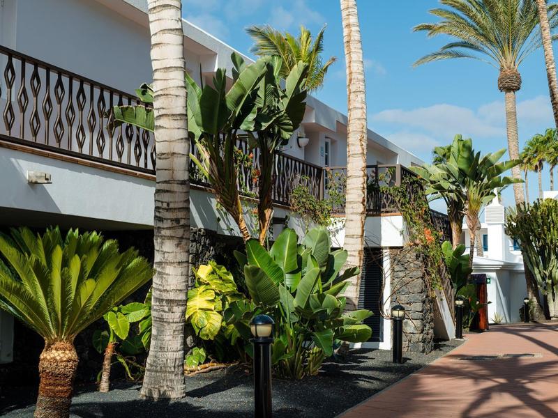 Esterno di hotel con palme, piante tropicali e balconi sotto un cielo blu