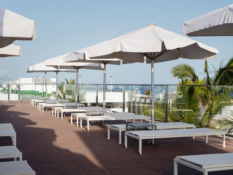 Lettini prendisole sotto ombrelloni su una terrazza dell'hotel con vista sull'oceano in una giornata di sole.