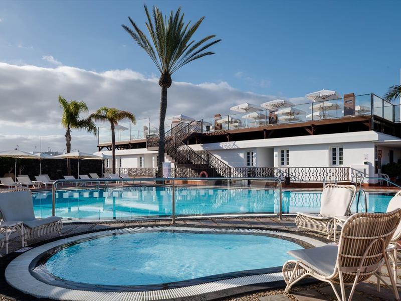 Area piscina esterna con sdraio, ombrelloni e palme in un hotel soleggiato.