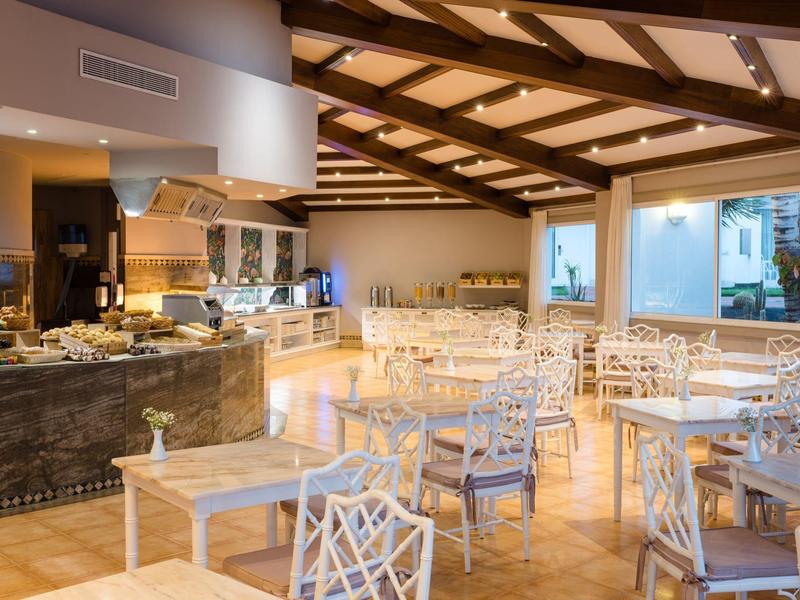 Elegante sala pranzo dell'hotel con sedie bianche, tavoli in legno e grandi finestre sotto travi di legno.