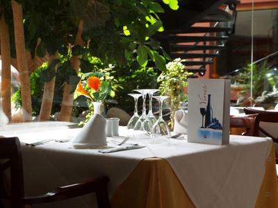 Tisch mit weißen Tüchern, Weingläsern, Menü und roter Rose in hellem, gemütlichem Restaurant.