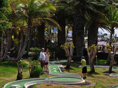 Park mit großen Palmen, grünem Minigolfplatz und Menschen, die Minigolf spielen.