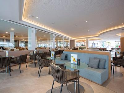 Modernes Restaurant mit hellen Möbeln, grauen Sesseln und großem, offenem Raum mit indirekter Beleuchtung.