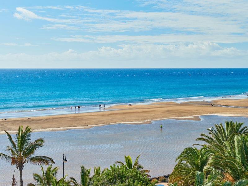 Spiaggia con palme, mare blu e sabbia chiara sotto un cielo parzialmente nuvoloso
