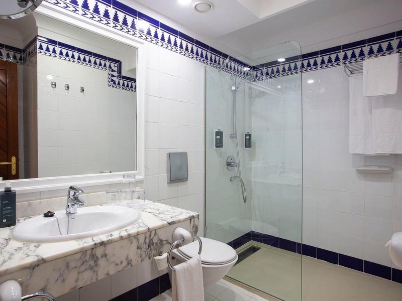 Bagno moderno con lavabo in marmo, ampia doccia e piastrelle bianche con accenti blu.