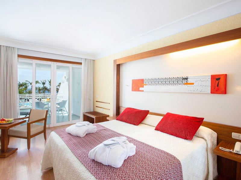 Camera d'hotel moderna con letto matrimoniale, balcone e pavimento in legno, arredi luminosi e accoglienti.