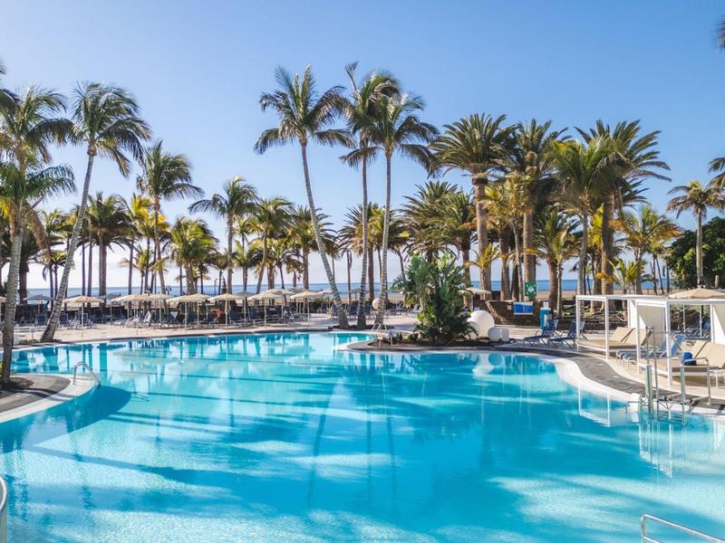 Acqua limpida blu della piscina con palme e ombrelloni sotto un cielo limpido