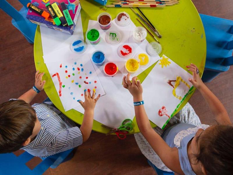 Due bambini dipingono con le dita a un tavolo verde usando vari colori vivaci.