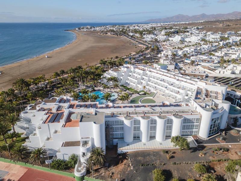 Grande edificio dell'hotel sulla costa con piscina e spiaggia in un paesaggio soleggiato e secco.
