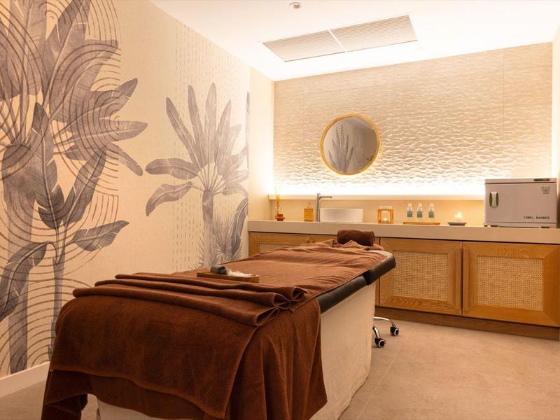 Stanza tranquilla per massaggi o trattamenti con lettino imbottito e tonalità calde marroni e beige.