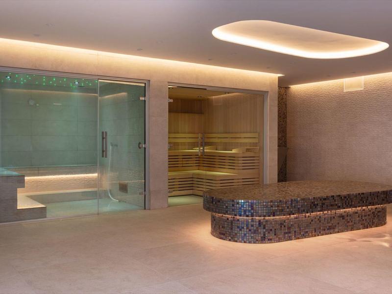 Area spa moderna con sauna, bagno turco e tavolo relax illuminato.
