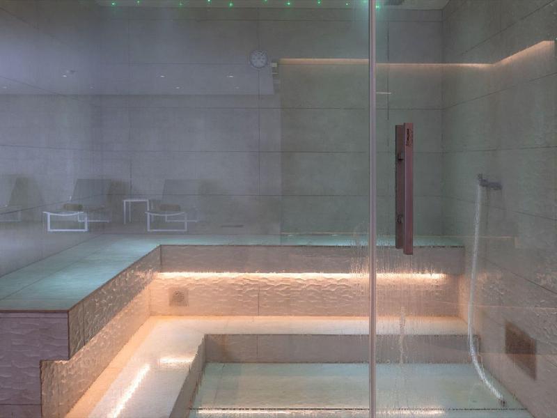 Sauna moderna con pareti in vetro, panchine in legno e illuminazione indiretta