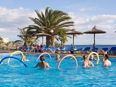 Ludzie ćwiczący aerobik wodny na hotelowym basenie z widokiem na morze i palmy