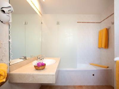 Salle de bains lumineuse avec baignoire blanche, grands miroirs et serviettes jaunes.