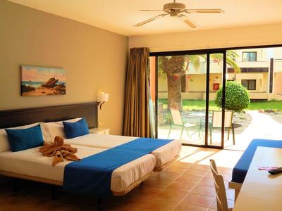 Chambre avec deux lits, accents bleus, télévision et accès à un jardin.