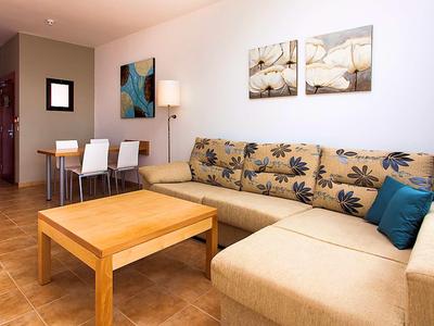 Salon confortable avec canapé beige, table en bois et coin repas avec chaises blanches.