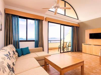 Salon lumineux avec canapé, table en bois et balcon avec vue sur la mer dans une chambre d'hôtel.