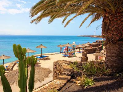 Plage avec parasols, palmiers et vue sur la mer bleue sous un ciel dégagé.