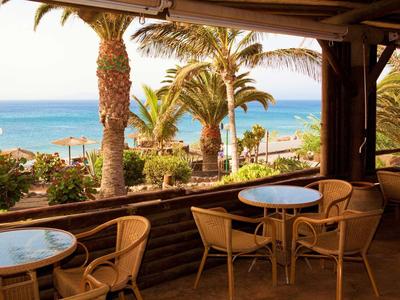 Terrasse avec tables et chaises donnant sur des palmiers et la mer en arrière-plan.