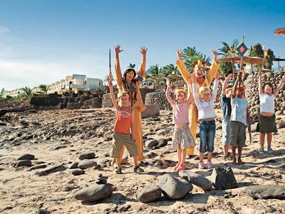 Groupe d'enfants heureux avec les bras levés sur une plage rocheuse sous un ciel bleu